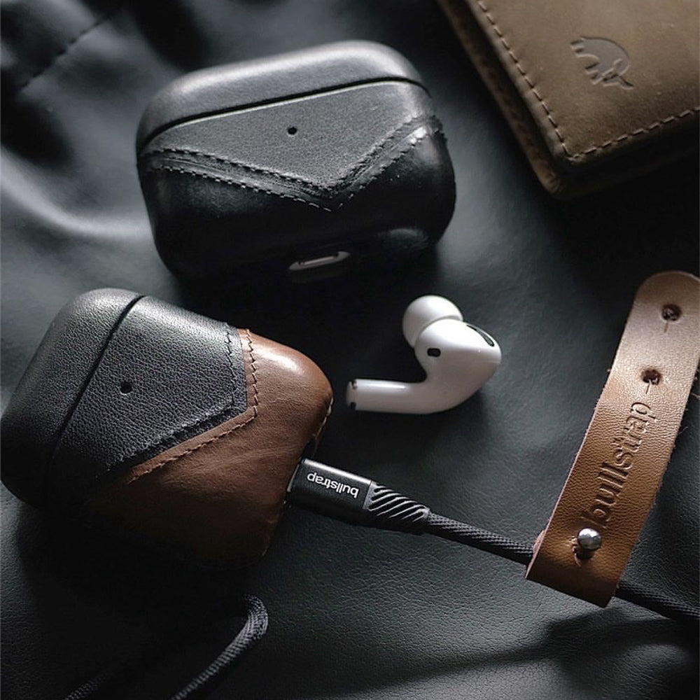 Two leather AirPods cases (black and brown), an AirPods Pro earbud, and a charging cable with bullstrap leather strap