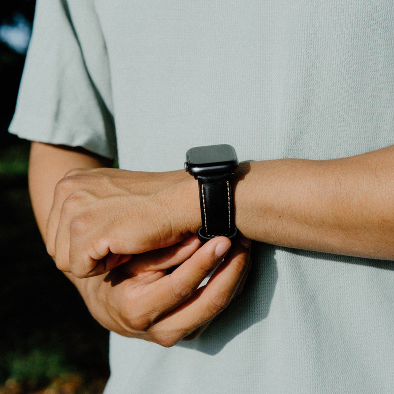 A person adjusting a leather Apple Watch strap on their wrist.