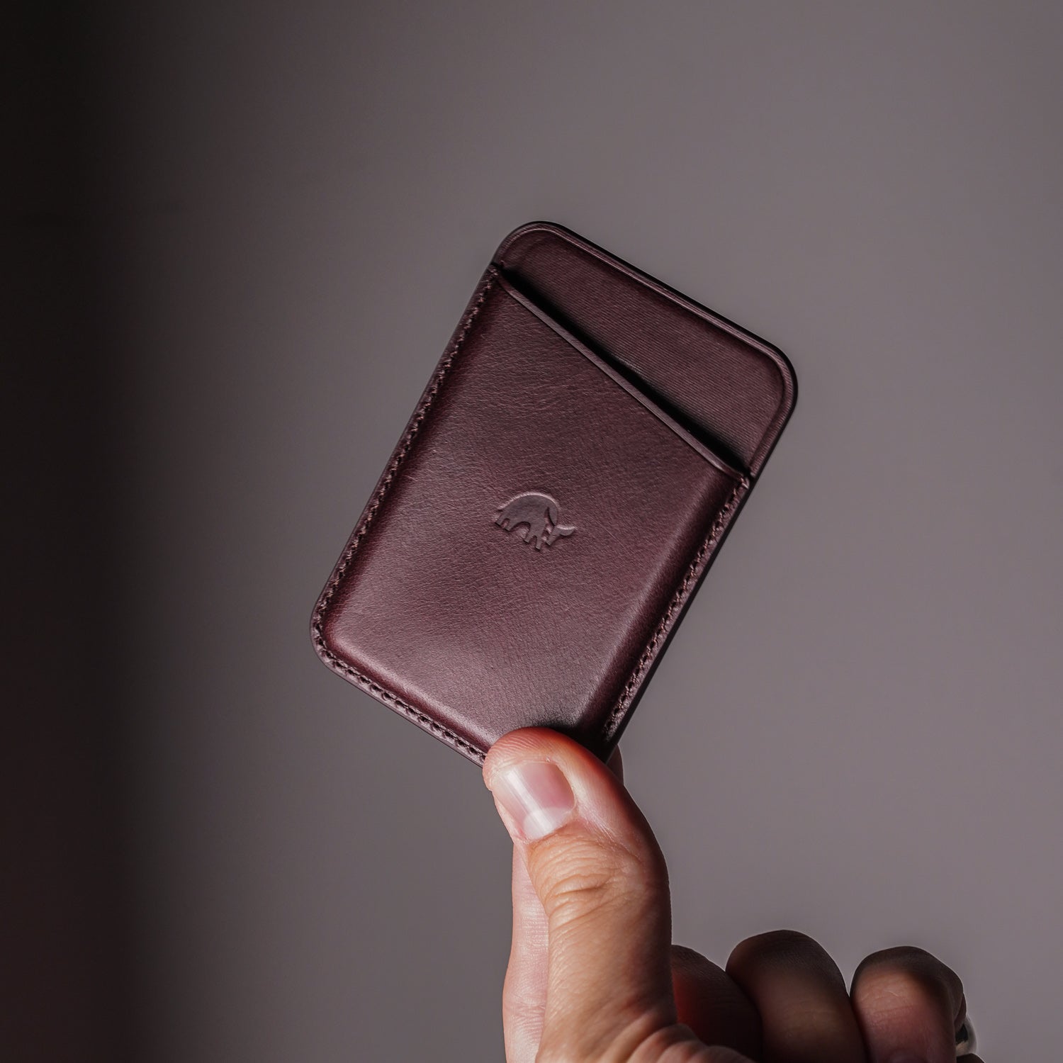 A hand holding a Leather Magnetic Wallet in Bourbon color, showcasing its card slots and embossed logo.