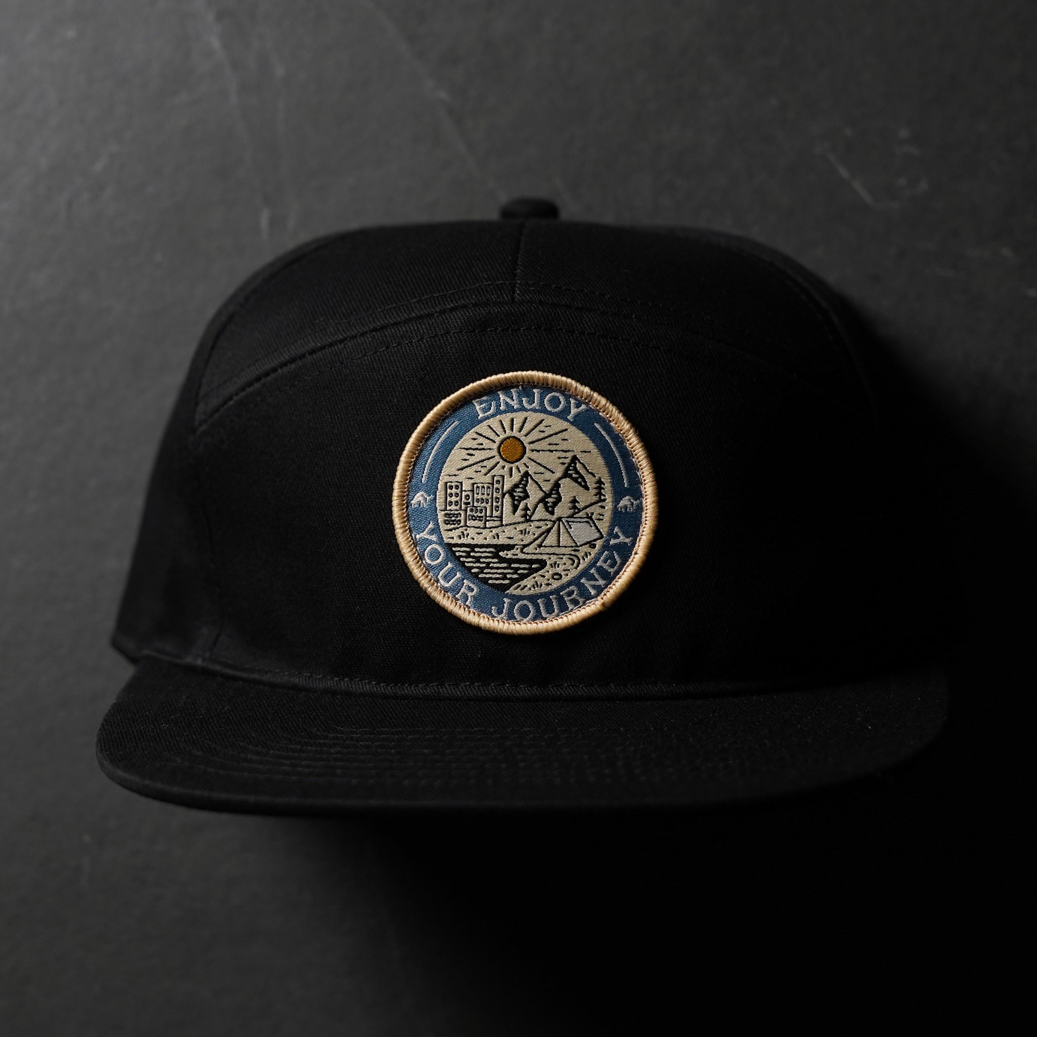Black hat with an embroidered badge that says 'ENJOY YOUR JOURNEY'