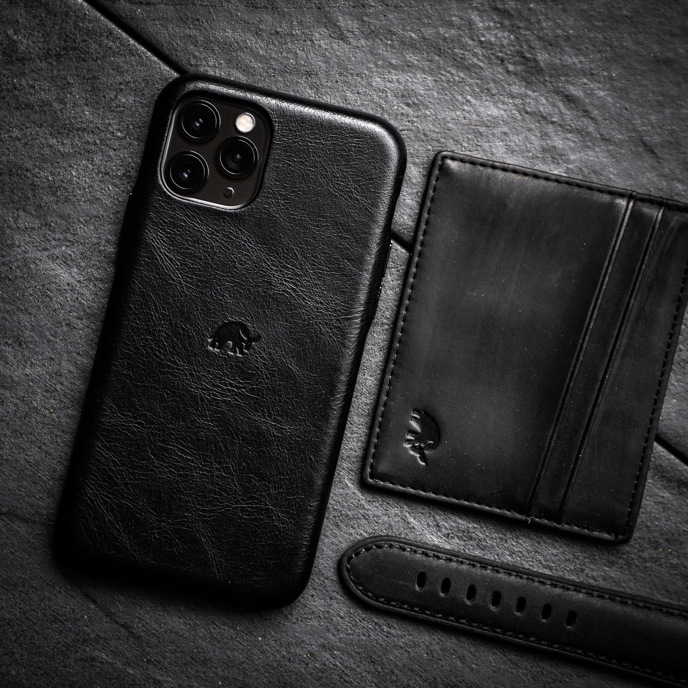 Black leather card holder next to a phone case and strap on a dark surface