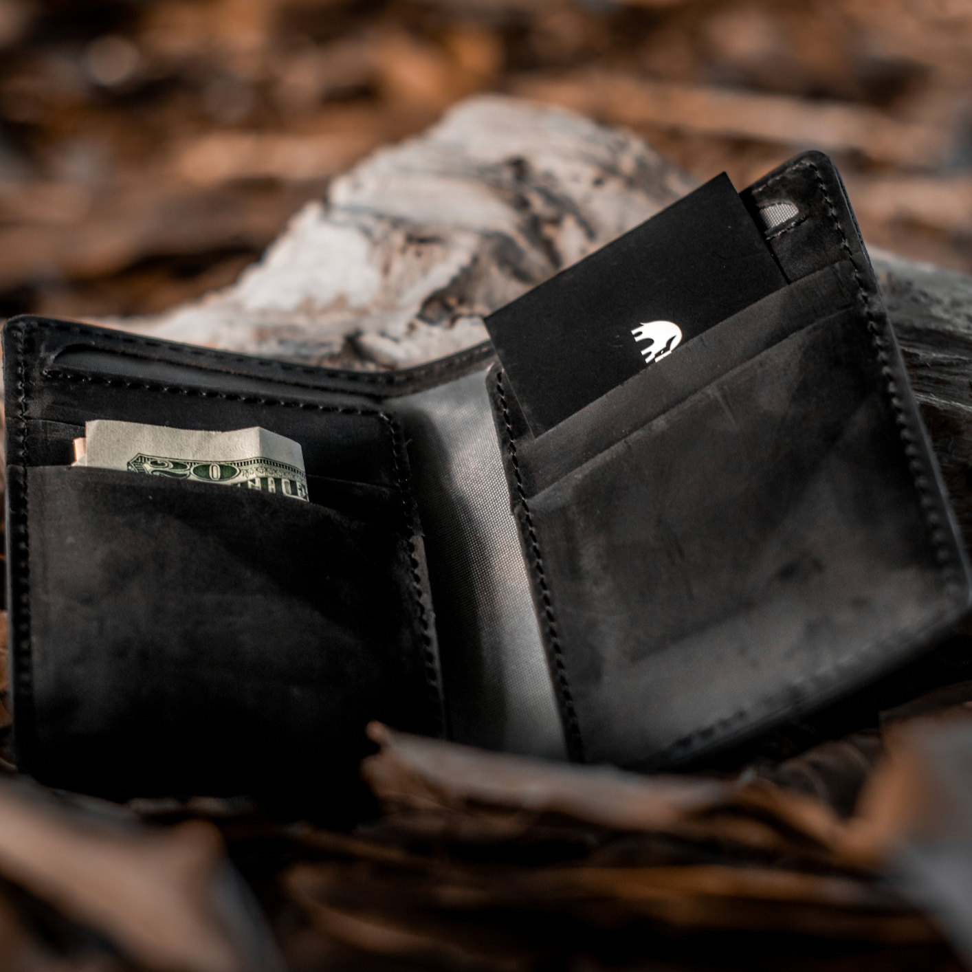Open black leather wallet with folded 20 bill visible and a black card showing a white logo.