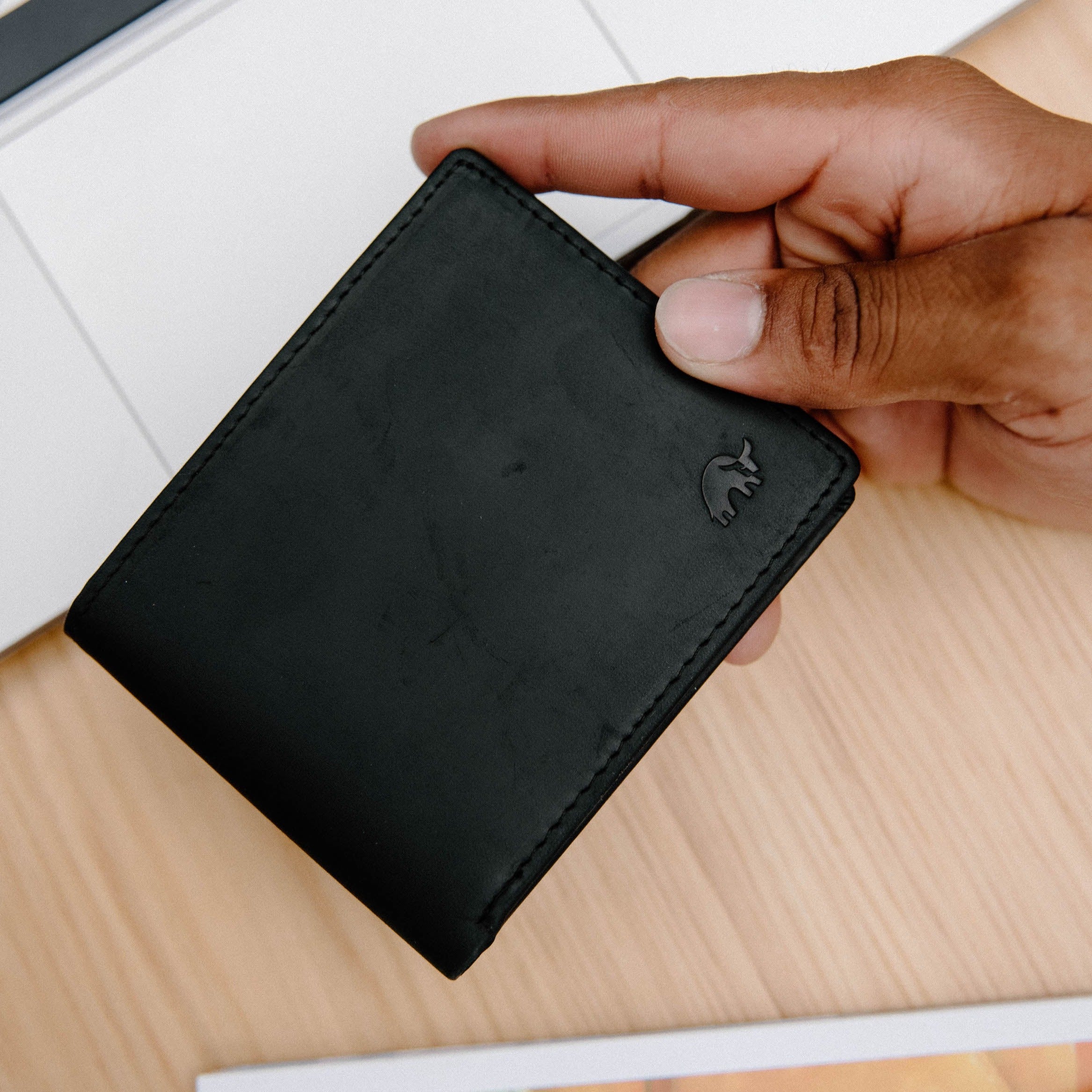 A person holding a black bifold wallet with embossed logo.