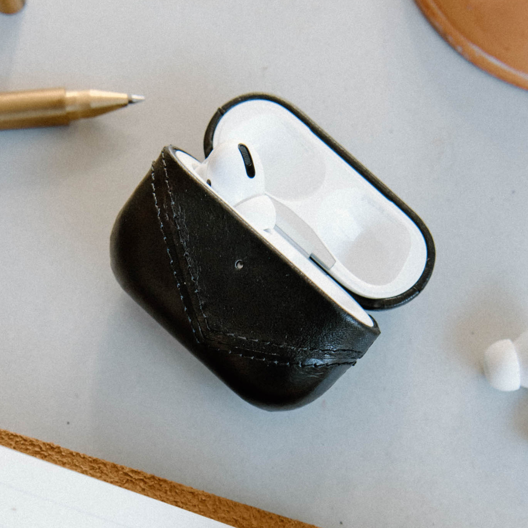 Black leather AirPods case with AirPods inside, showing the lid open.