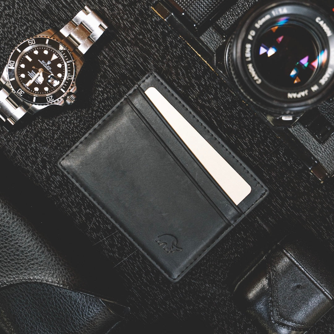 Black leather card holder with a card and a watch and camera in the background