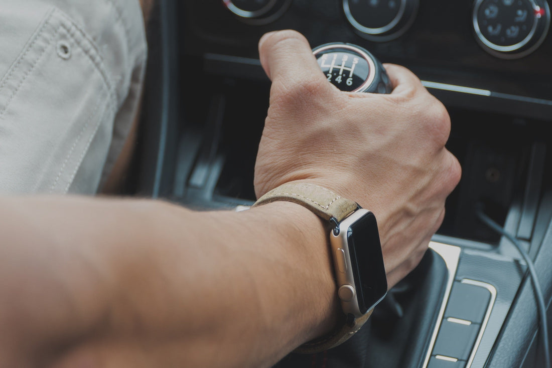 Close-up of a hand gripping a gearshift, wearing a leather Apple watch band.