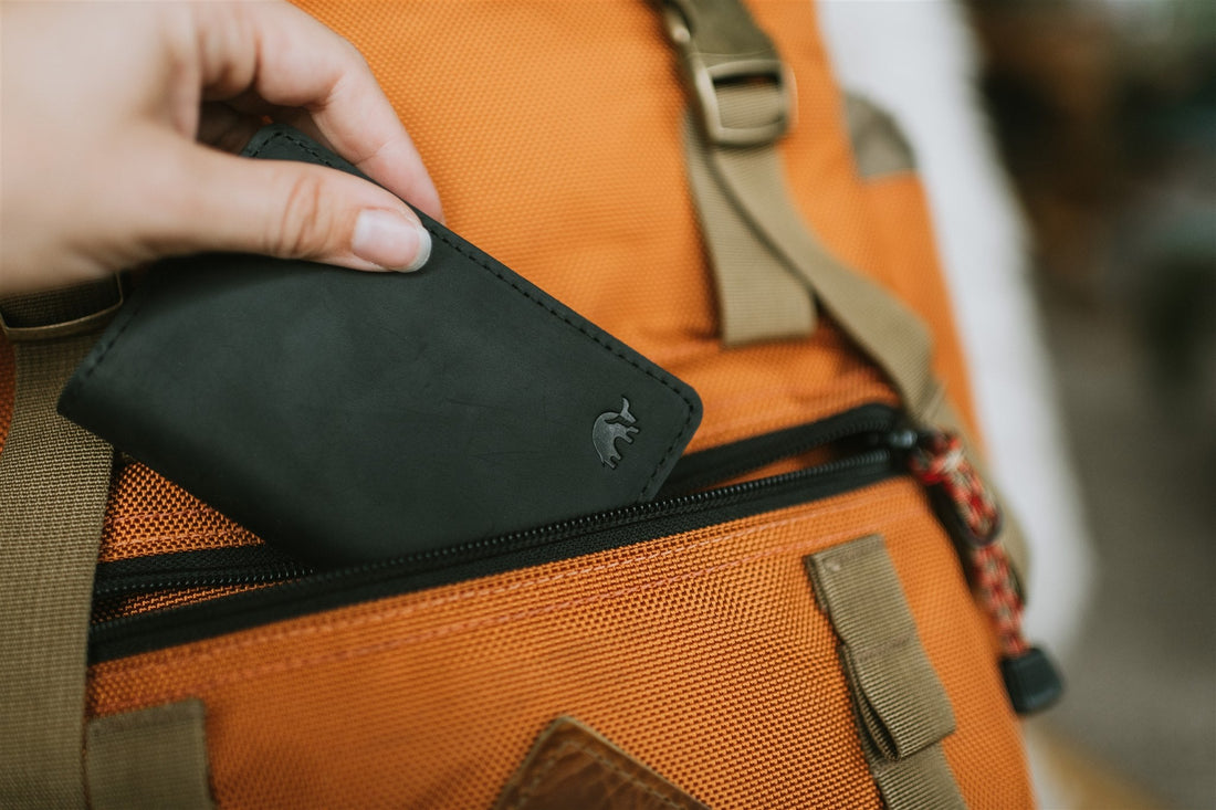 A black leather wallet being placed into an orange backpack pocket