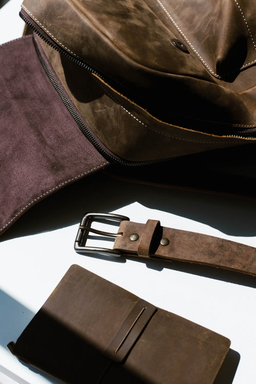 A brown leather bag with a belt and notebook on a table.