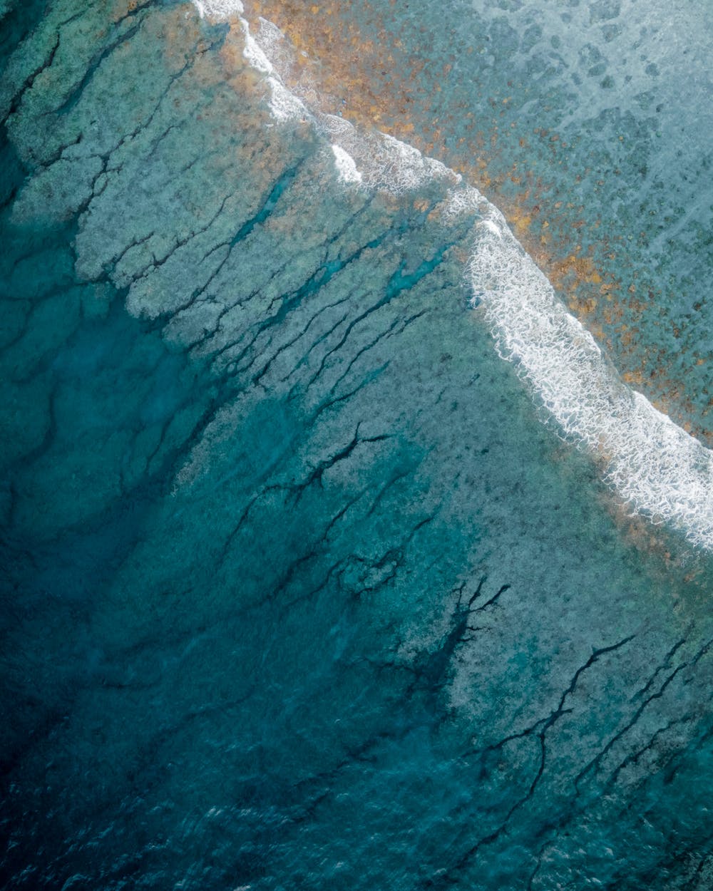 Aerial view of ocean waves breaking over a coral reef with blue and turquoise water.