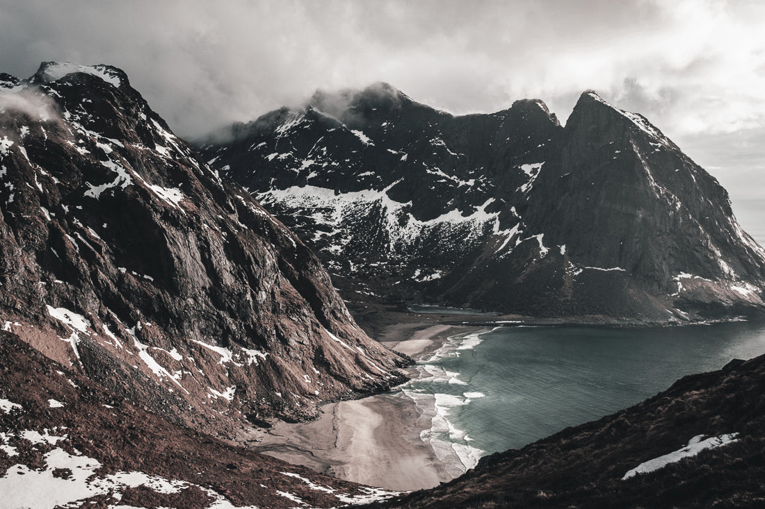 A scenic view of mountains and a beach with snow and clouds