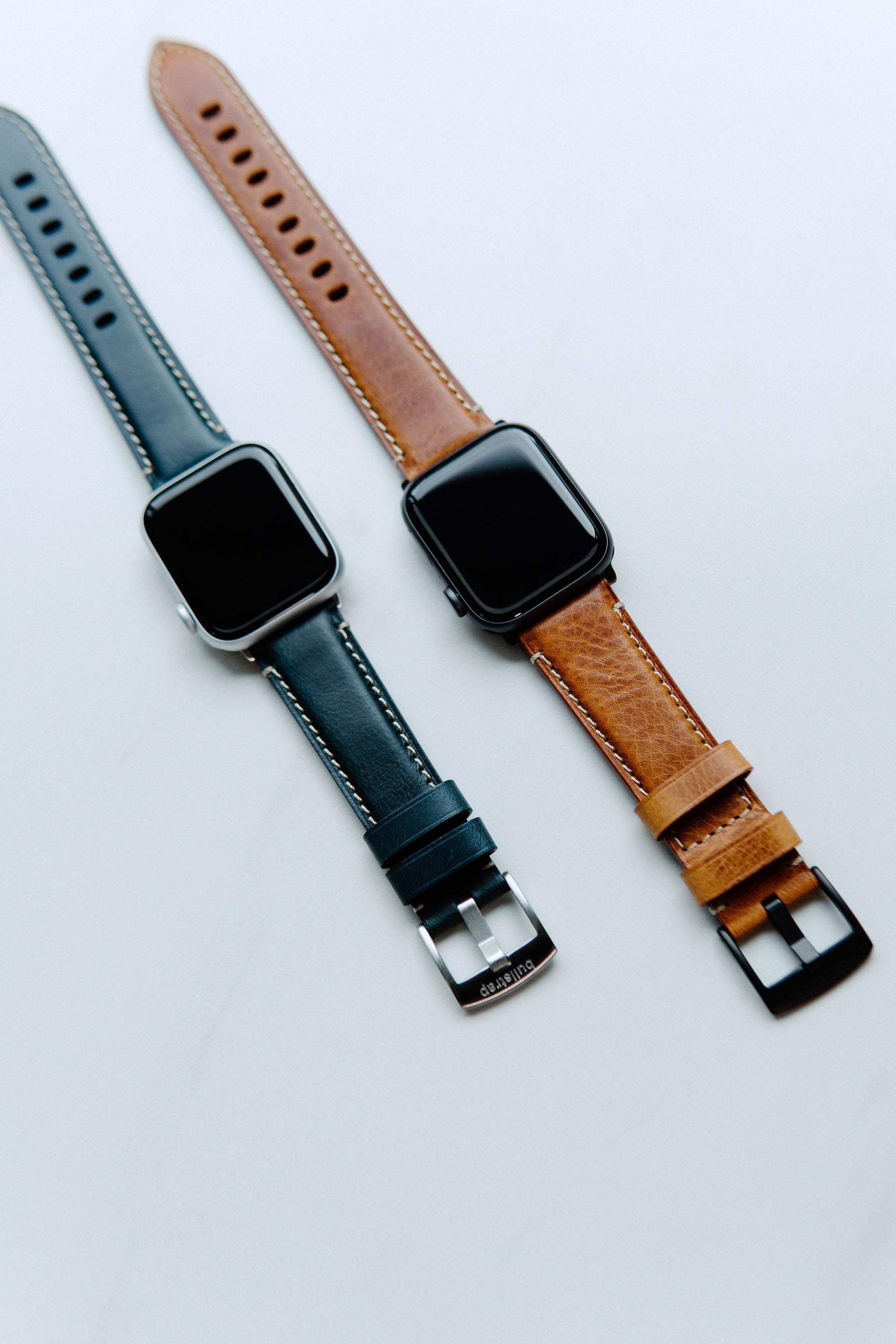 Two smartwatches with stitched leather straps, one sienna brown and one ocean blue