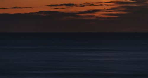 A sunset over the ocean with clouds and waves