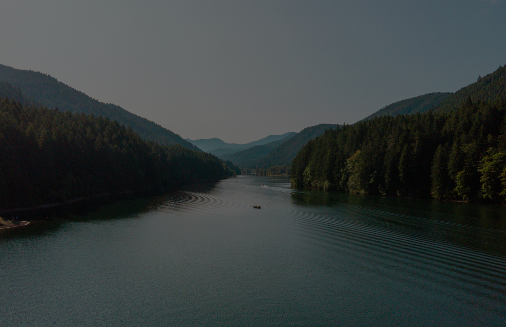 A serene landscape view of a river surrounded by mountains and forests.