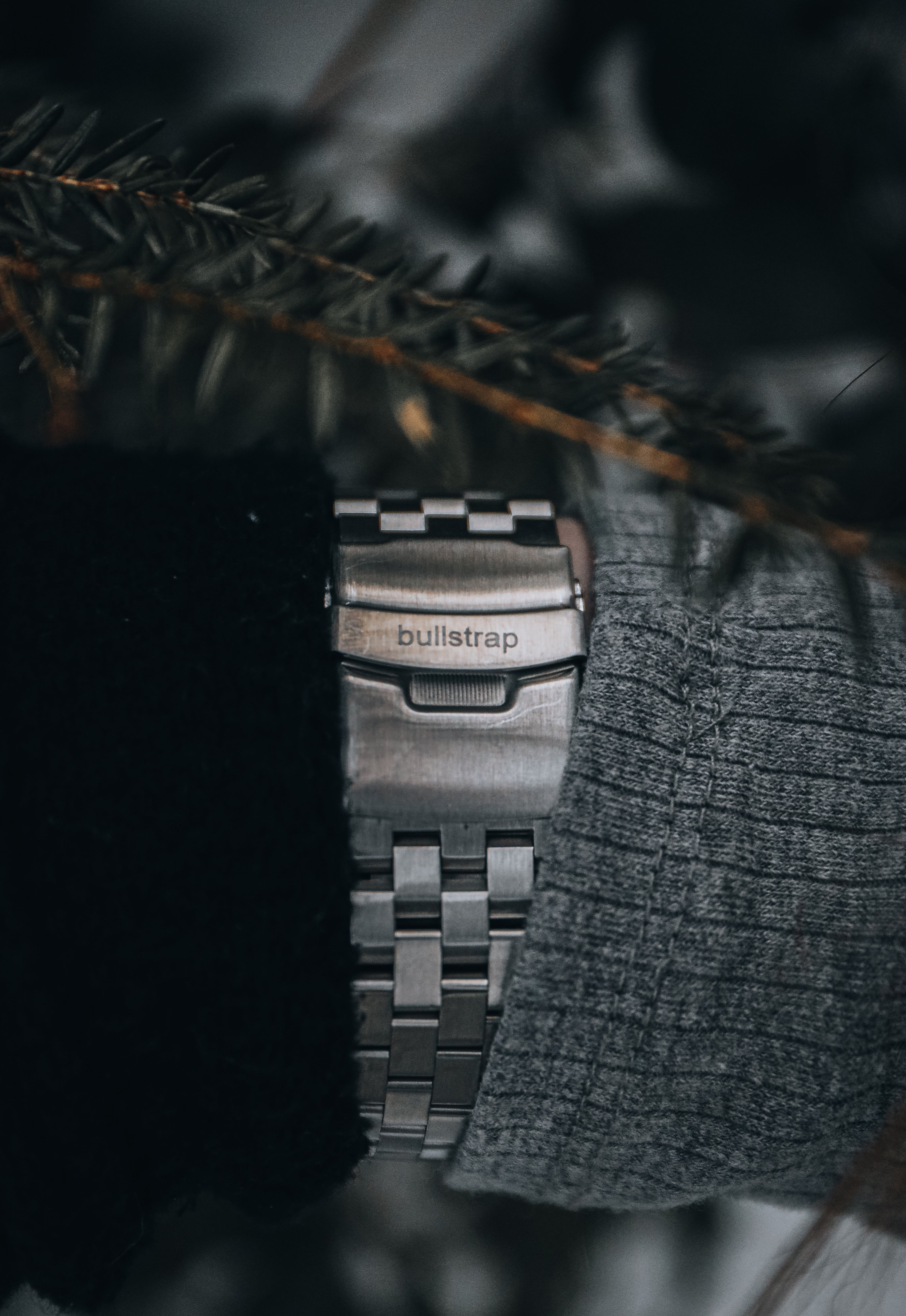 Stainless steel watch bracelet clasp engraved bullstrap, worn between dark jacket and gray sweater sleeves