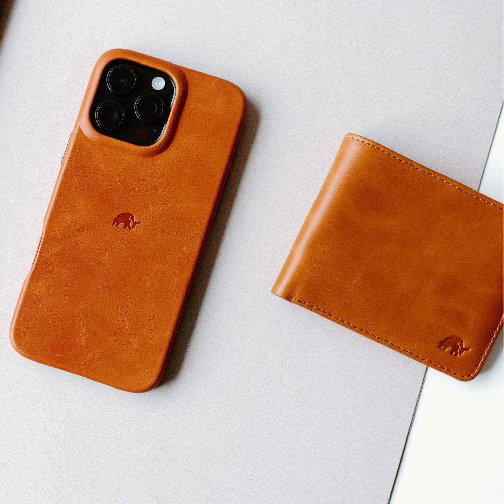 Tan leather iPhone case with embossed logo and matching tan leather bifold wallet on light gray surface.