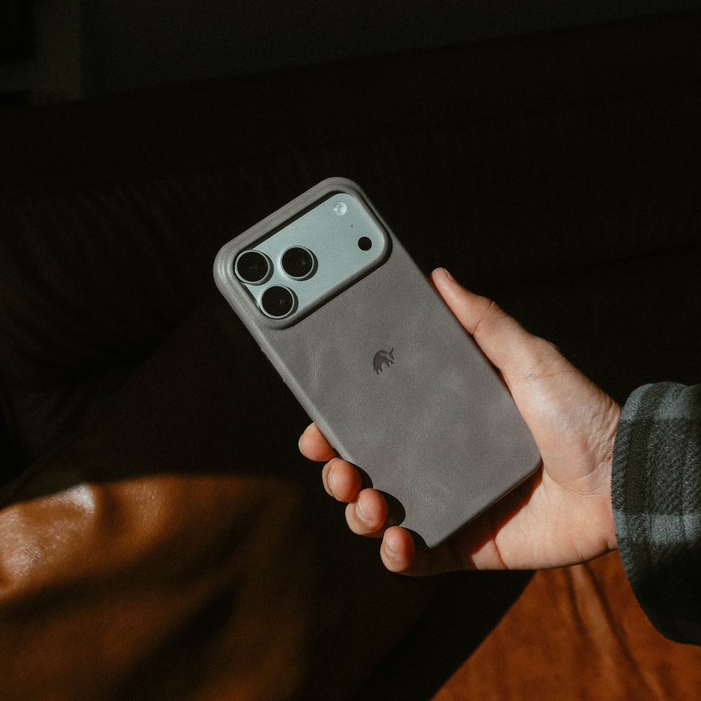 Hand holding a gray leather iPhone case with triple camera cutout and small Bullstrap logo.