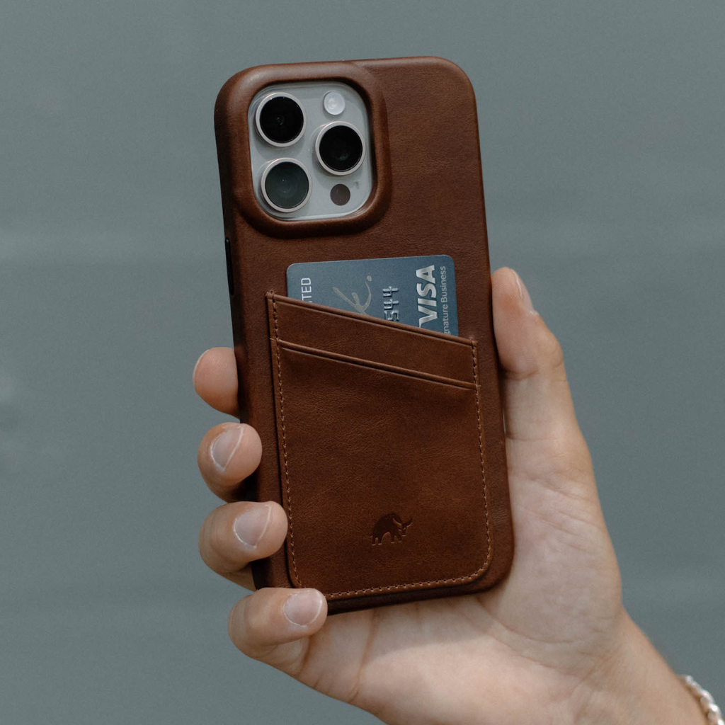 A hand holding a brown leather iPhone case with a card in the pocket.