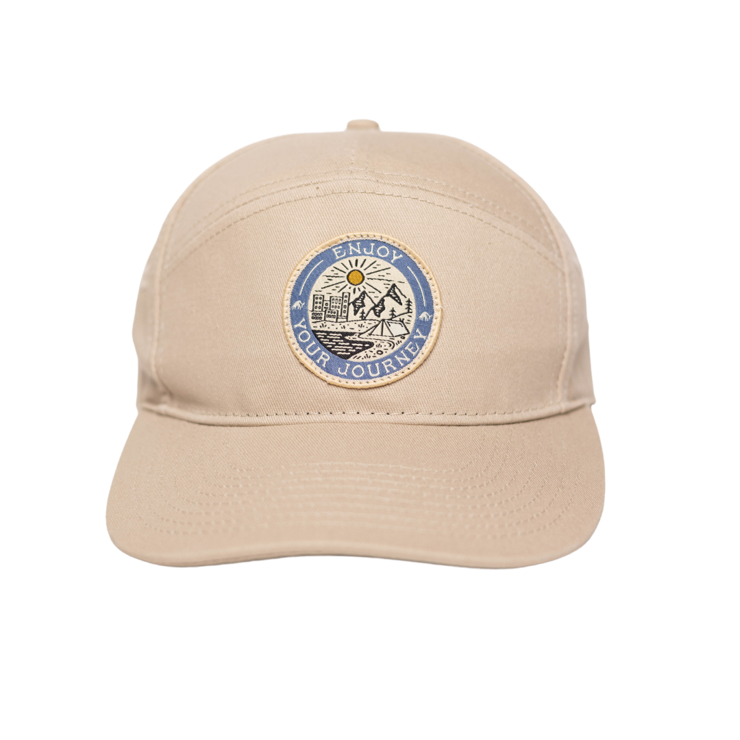 Beige baseball cap with round patch reading 'ENJOY YOUR JOURNEY' and mountain, sun, and tent illustration