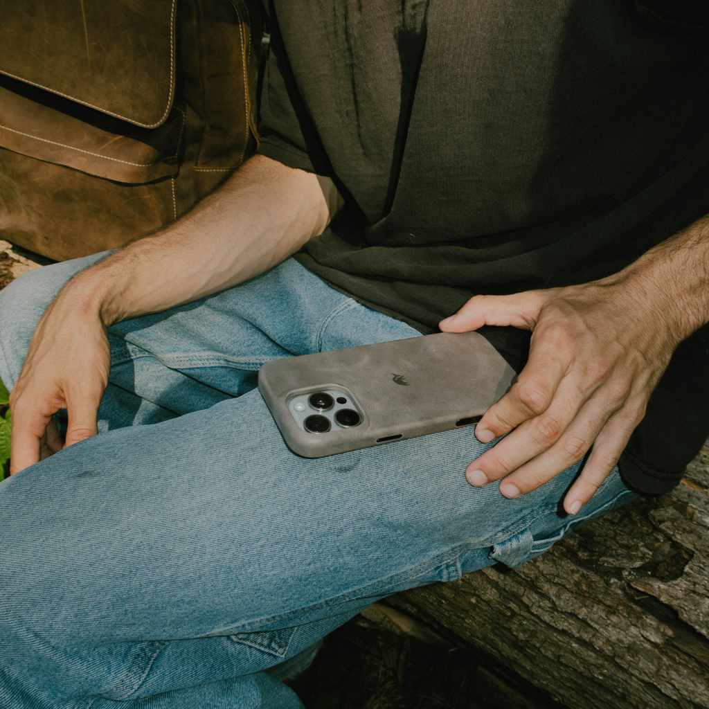 Slate leather minimalist iPhone case resting on a person's lap wearing jeans, hands visible nearby.