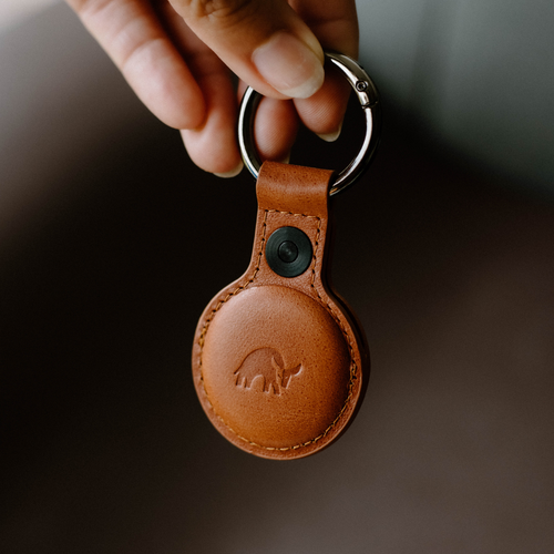A hand holding a BullTag for AirTag in sienna leather with a keyring attachment.