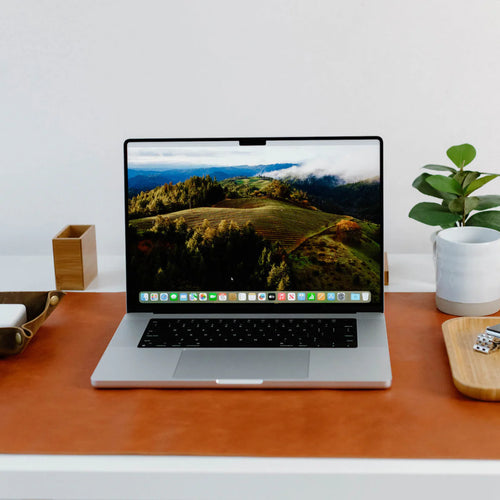 Laptop and desk accessories arranged on a brown leather desk mat