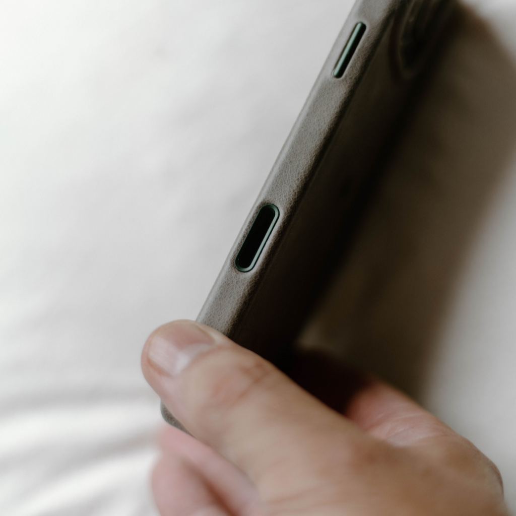 Close-up of a hand holding a slate-gray minimalist phone case showing side port cutouts and textured finish
