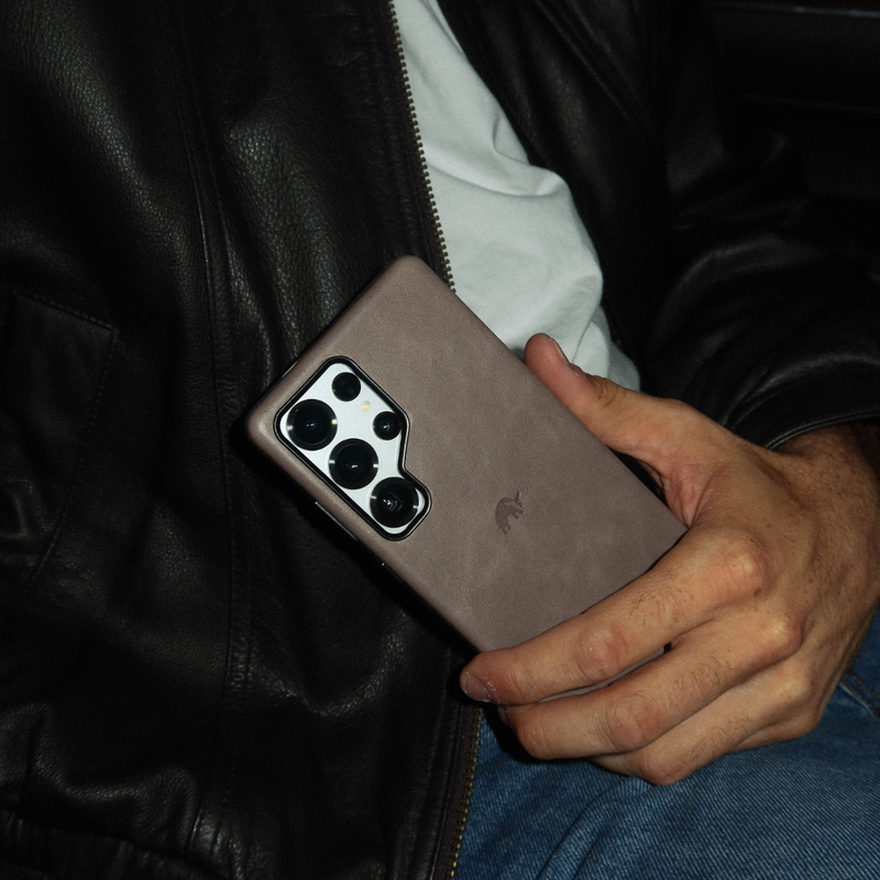 Back view of slate Samsung Galaxy S25 Ultra case showing camera cutout and embossed logo held against black leather jacket
