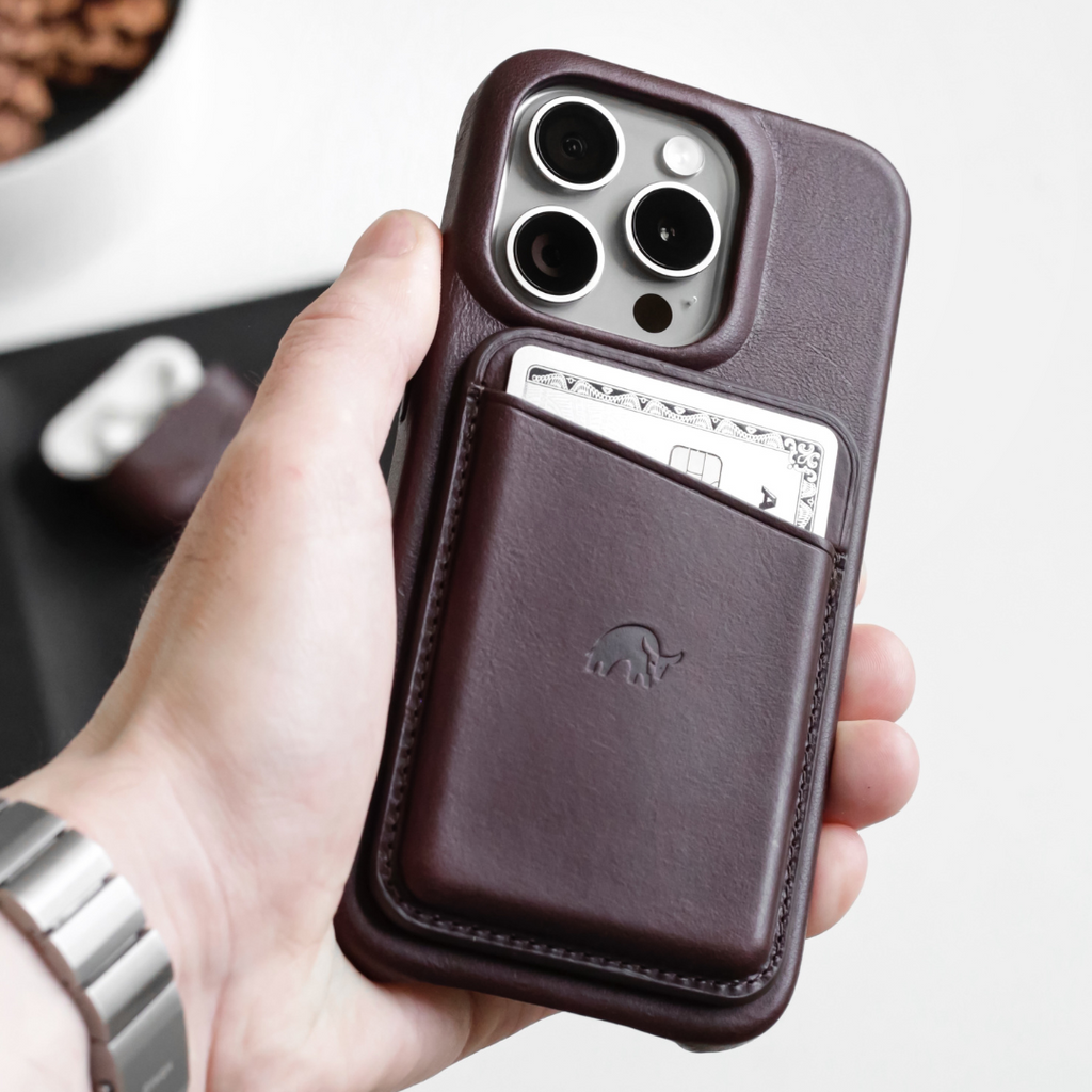Hand holding iPhone with bourbon-brown leather case and slim card pocket showing an embossed elephant logo.
