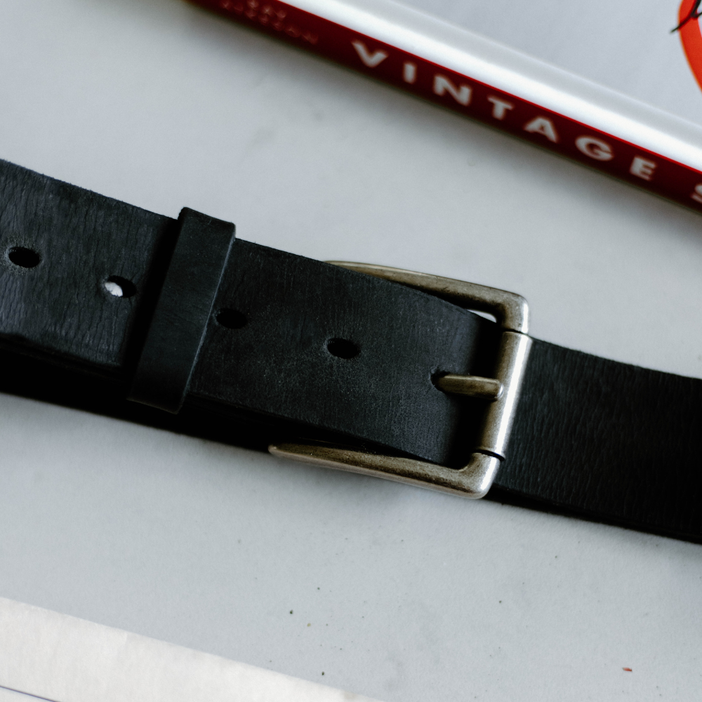 Close-up of black leather belt with metal buckle on a table; red book spine reads 'VINTAGE'.