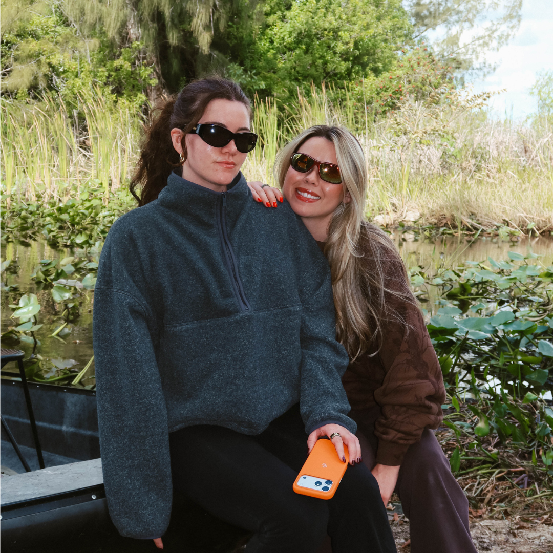 Two women sitting by a pond, one holding an iPhone with a hunter orange Blaze leather case