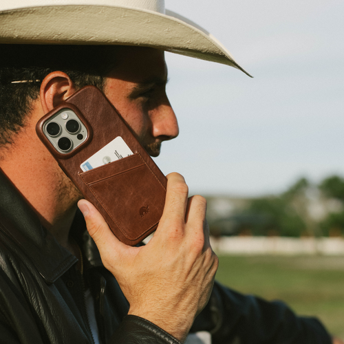 Man in cowboy hat holding a brown leather minimalist portfolio phone case with a card in its back pocket