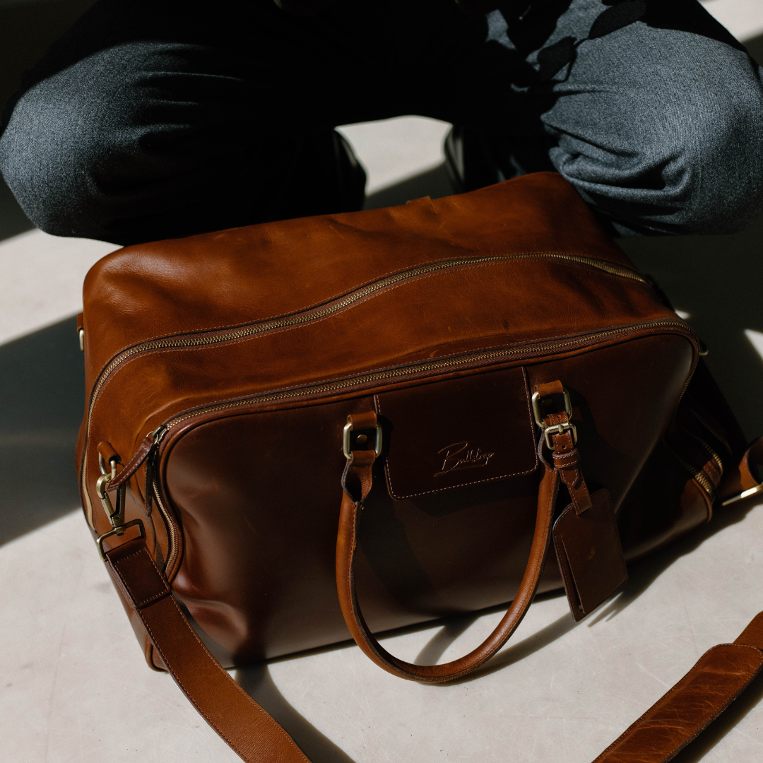 Front three-quarter view of Bullstrap Odyssey travel bag in brown leather with brass hardware and zippered front pocket