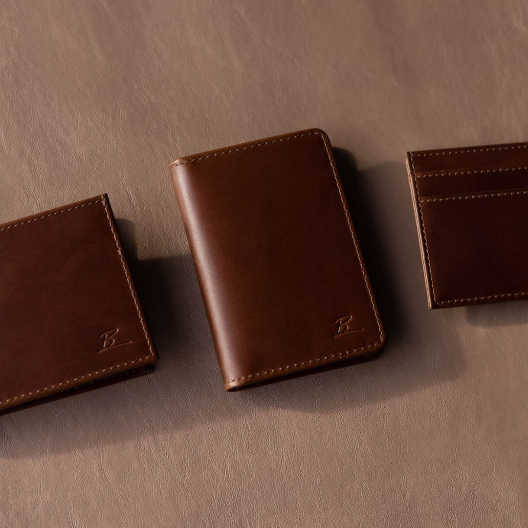 Three brown leather wallets and cardholder on a tan leather surface, each embossed with a 'B' monogram.