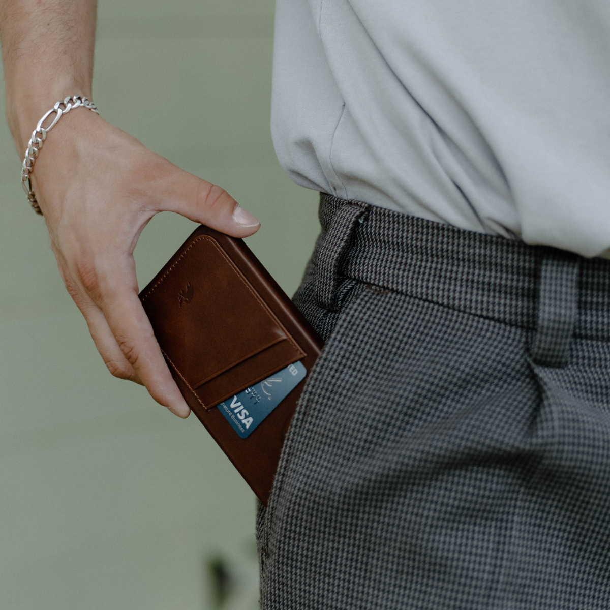 Hand sliding brown Terra Minimalist Portfolio Case into trouser pocket, showing exterior card slot and slim profile