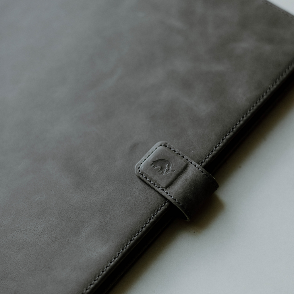 Close-up of a slate leather iPad case with a logo and strap