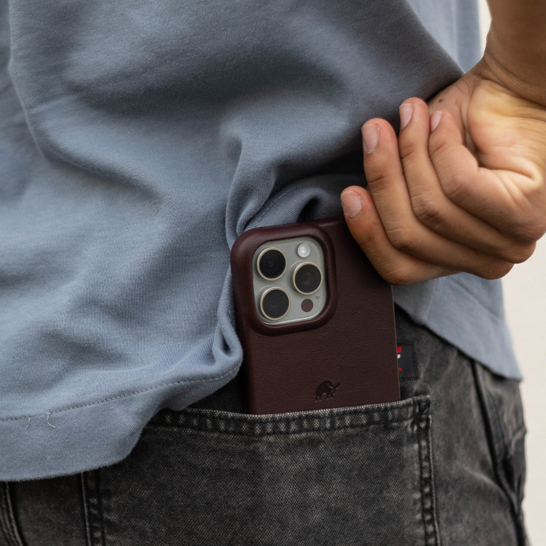 Burgundy leather iPhone case partially in back pocket of jeans, phone camera visible as hand tucks shirt hem
