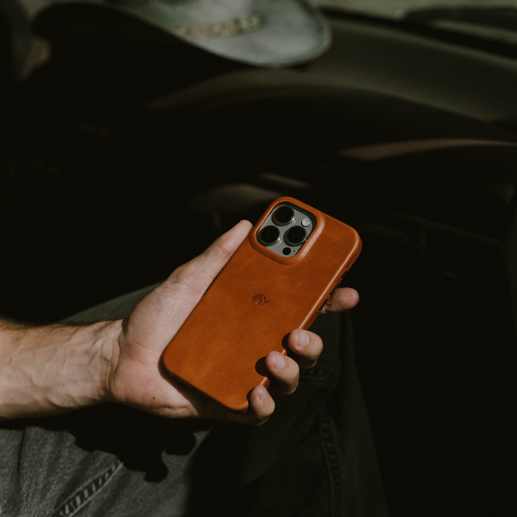 Hand holding iPhone with sienna leather case showing triple-camera cutout