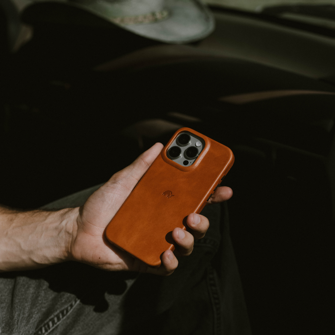 Hand holding iPhone with sienna leather case showing triple-camera cutout