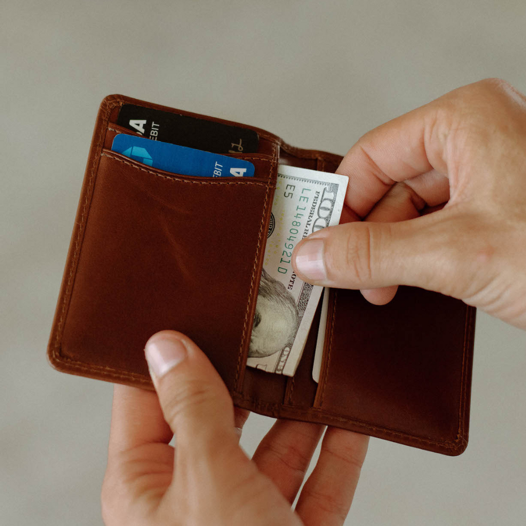 Brown minimalist leather wallet with cards (DEBIT) and folded bill serial LE1480492D E5 being removed by hand