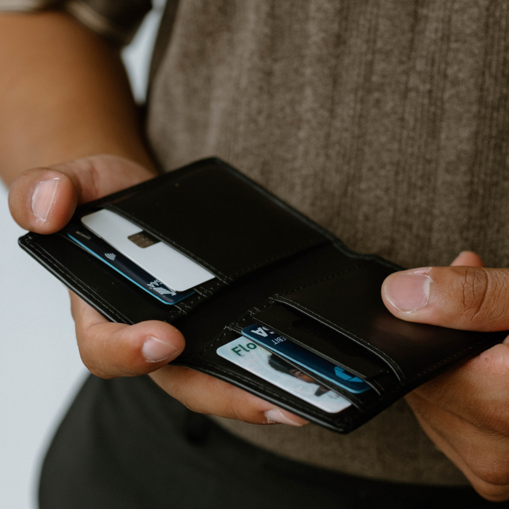 Hands holding open black leather bifold wallet showing card slots and a card labeled FLO