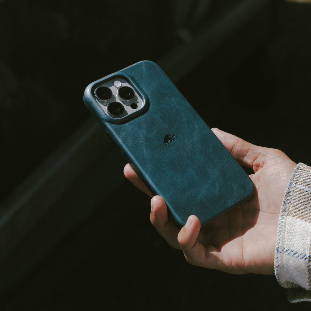 Teal leather phone case held in hand showing triple-camera cutout and small embossed rhino logo