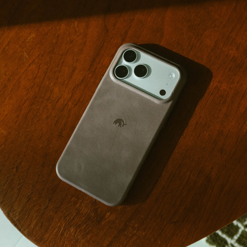 Angled view of Contemporary Plateau Slate leather iPhone case showing raised camera lip and embossed Bullstrap logo on wood table