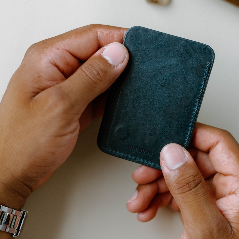 A person holding a dark teal leather wallet with the Bullstrap logo visible.