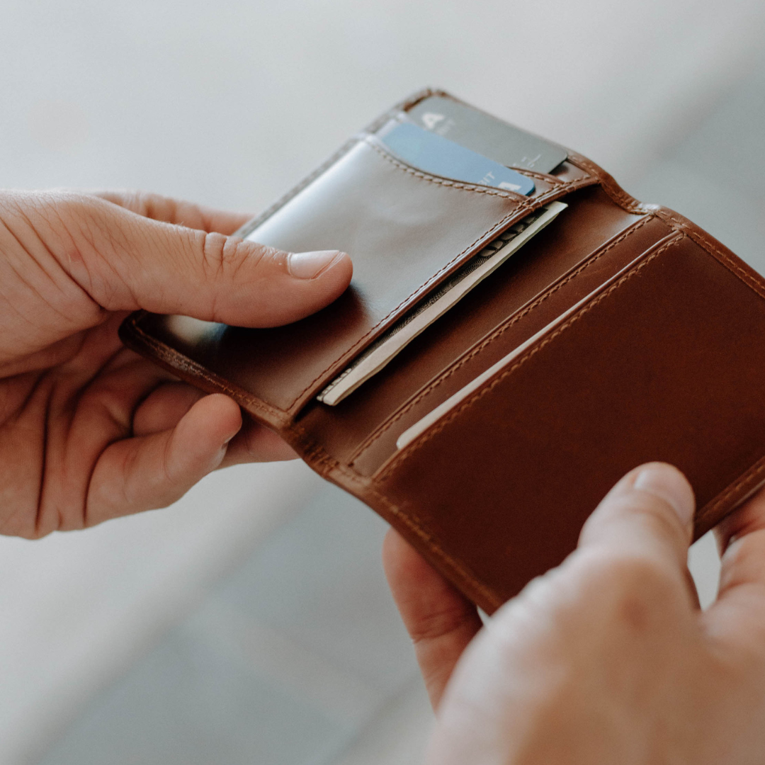 Brown leather minimalist wallet held in hands, showing card slots with cards and folded cash