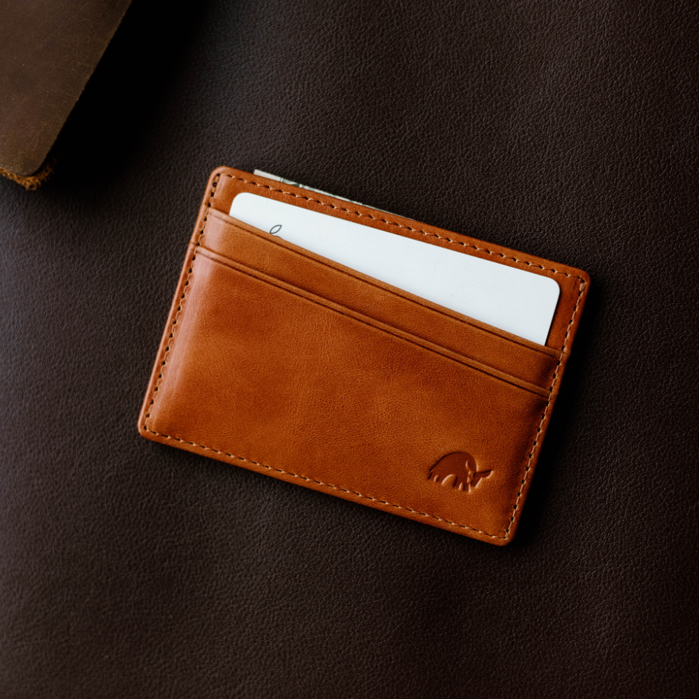 Tan leather card wallet with a white card partially inserted, on a dark brown leather surface.