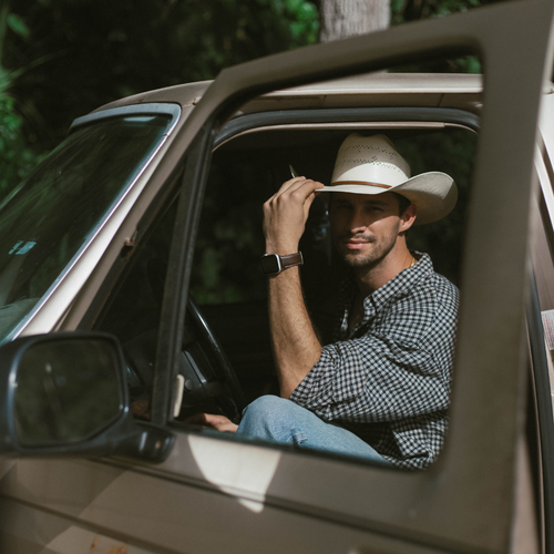 Man in cowboy hat sitting in pickup, showing leather Apple Watch strap 'Modern Terra' on his wrist.