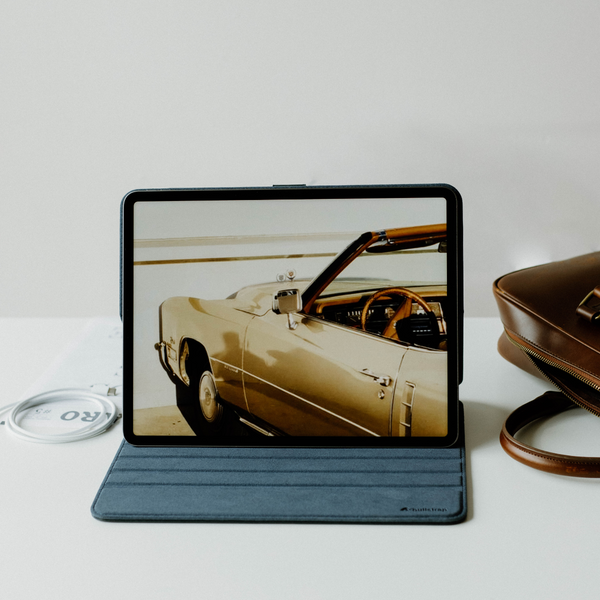 Tablet on a stand showing a vintage gold convertible car photo; 'RO' visible on a disc beside it, and a brown leather bag.