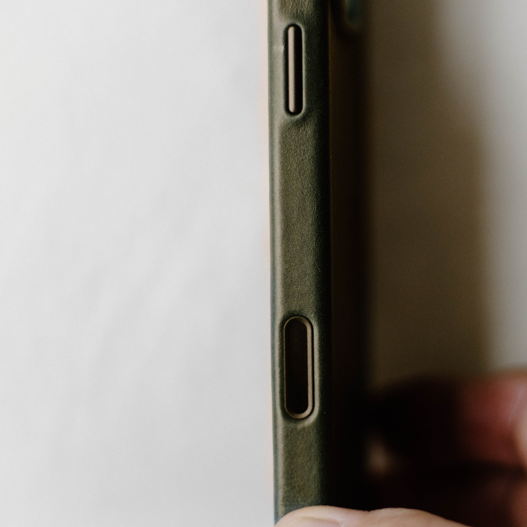 Close-up of an olive-green phone case edge showing volume button cutout and side port, fingertip holding bottom