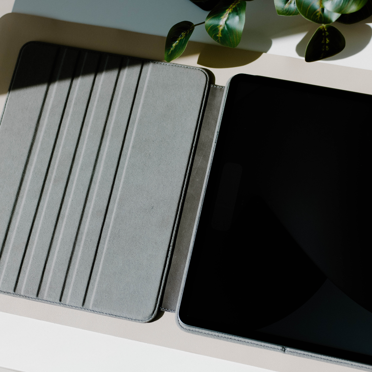 Open leather iPad case in slate color, showing interior and device compatibility.