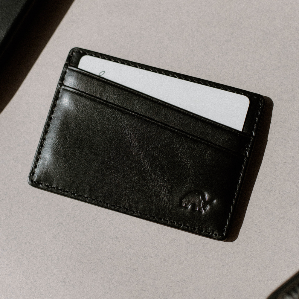 Black leather cardholder with a white card in the top slot and small embossed elephant logo on the lower right.